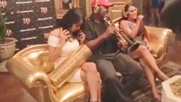 Women laughing on a gold couch next to a trumpet player at a Diddy party