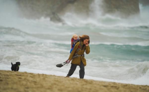 FALMOUTH, ENGLAND - SEPTEMBER 20: A woman takes a child and dog for a walk in front of stormy waves at Gyllyngvase Beach on September 20, 2023 in Falmouth, England. Parts of England are experiencing strong winds and heavy rain this week, with some reports of flooding, as a warm September gives way to autumn. (Photo by Hugh R Hastings/Getty Images)