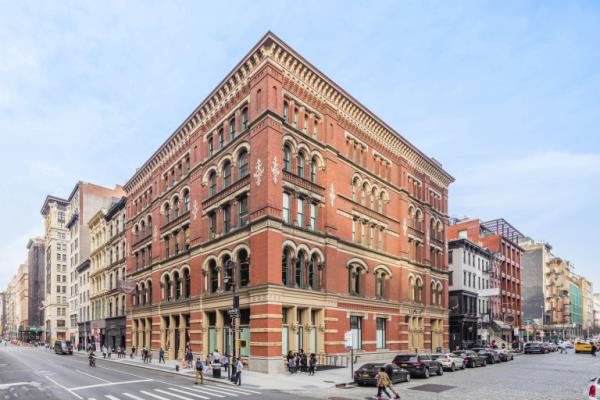 A large brick commercial building with multiple windows, part of Current Real Estate Advisors properties named Zero Bond, with people casually walking on the street.