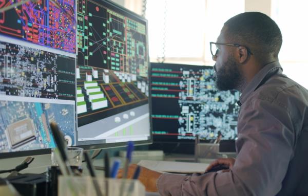A man sits before a large mo<em></em>nitor and looks at multiple windows on his computer.