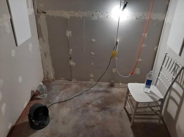 The cell includes a chair, water bottles and a single fan on the floor. 