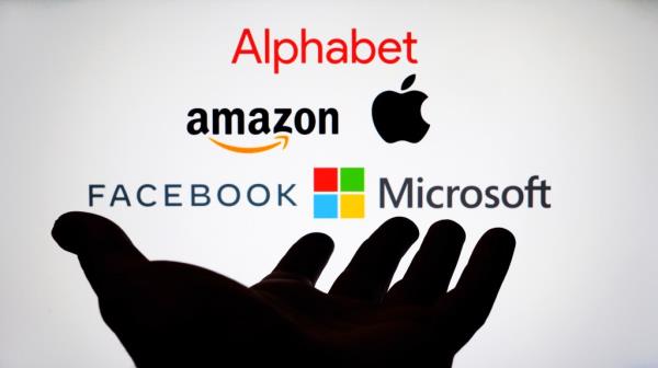 Logos for Alphabet, Amazon, Apple, Facebook and Microsoft displayed on screen with hand reaching towards them. Digital tax and antitrust concept.