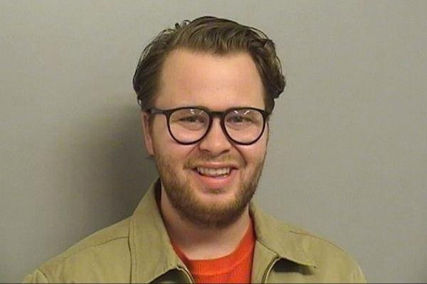 Alex Ray Scott with beard and beige suit smliing in mugshot