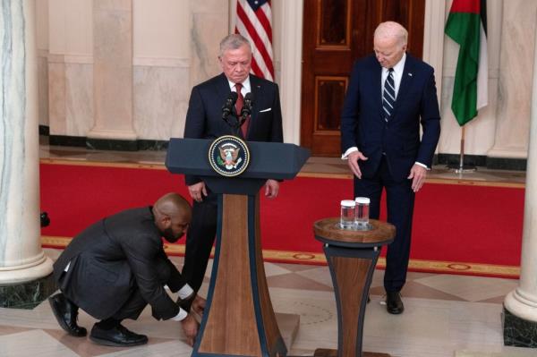 An aid places an apple box for King Abdullah II of Jordan (center) as he and US President Joe Biden deliver remarks during a press co<em></em>nference on Feb. 12, 2024. 
