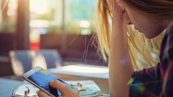 A young woman holding a broken smart phone with a sad look on her face