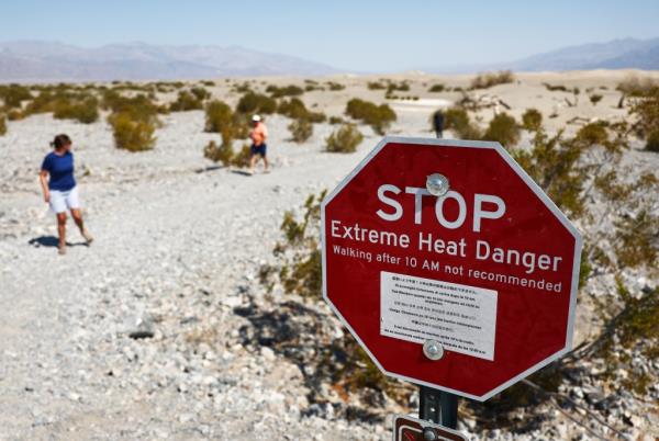 Visitors walk near a 'Stop Extreme Heat Danger' sign at Mesquite Flat Sand Dunes in the morning, when temperatures are less hot, during a long-duration heat wave which is impacting much of California on July 9, 2024 in Death Valley Natio<em></em>nal Park, California.