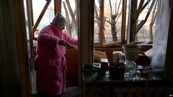 A woman sweeps broken windows glass in her flat after the explosion of a downed Russian drone in a yard among residential buildings in Kyiv, Ukraine, on Nov. 25, 2023. 