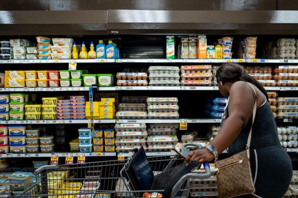 A customer pushes a cart while looking at eggs displayed in a grocery store
