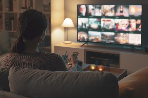 Woman relaxing on the couch, she is using the remote co<em></em>ntrol and choosing a TV show or movie on the television menu