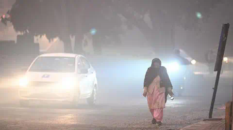 Getty Images A woman wearing a pink traditio<em></em>nal Indian dress and a black scarf walks along the side of the road in the early hours of the morning in Karol Bagh, Delhi, as vehicles pass by with their lights on due to low visibility.